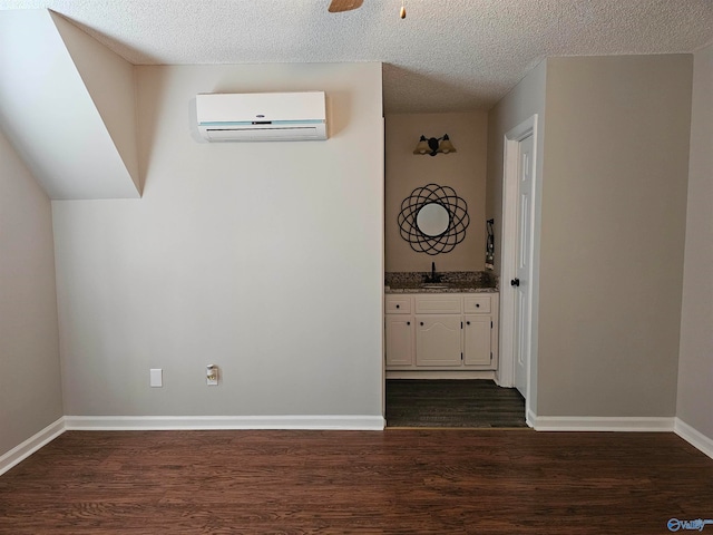 unfurnished room featuring a wall unit AC, dark hardwood / wood-style floors, sink, and a textured ceiling