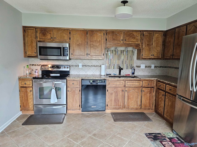 kitchen with light tile patterned floors, backsplash, stone countertops, sink, and stainless steel appliances