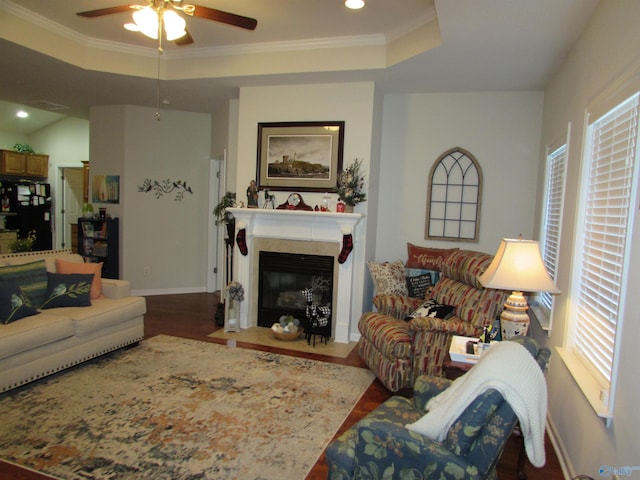 living area featuring dark wood-type flooring, a fireplace with flush hearth, baseboards, ornamental molding, and a tray ceiling