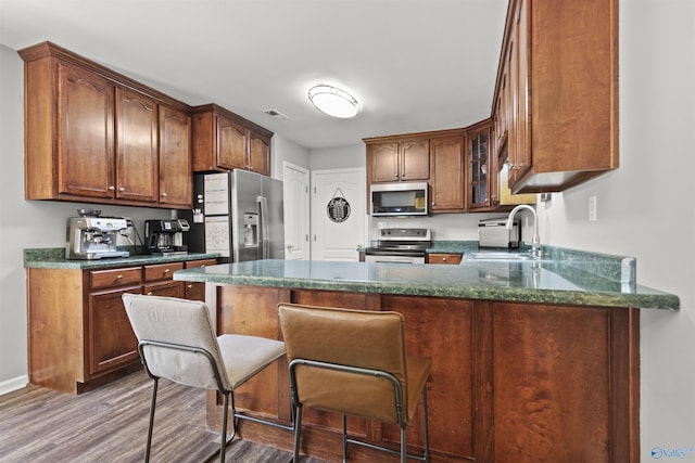 kitchen with a peninsula, a sink, visible vents, appliances with stainless steel finishes, and glass insert cabinets