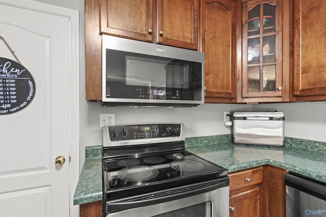 kitchen featuring appliances with stainless steel finishes, dark countertops, and glass insert cabinets