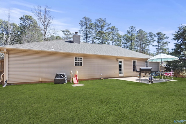 rear view of house with a shingled roof, a chimney, a patio, and a yard