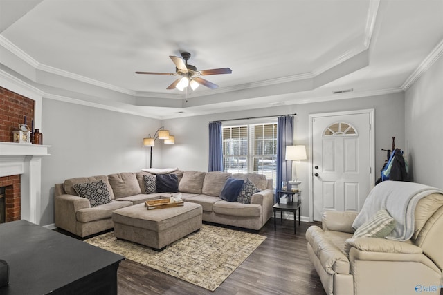 living area featuring a tray ceiling, dark wood-style flooring, visible vents, and a fireplace