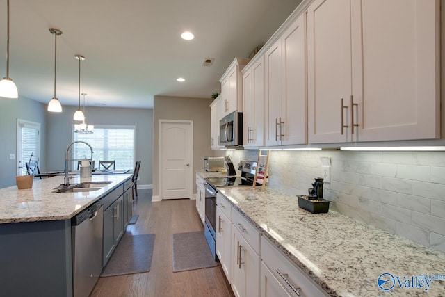 kitchen with white cabinets, decorative backsplash, wood finished floors, stainless steel appliances, and a sink