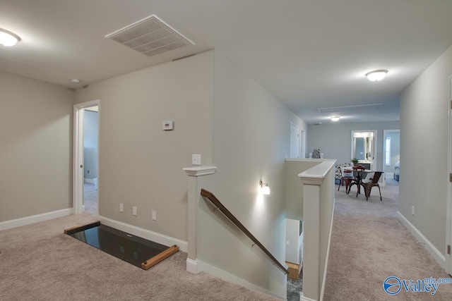 hallway featuring attic access, visible vents, carpet flooring, and an upstairs landing