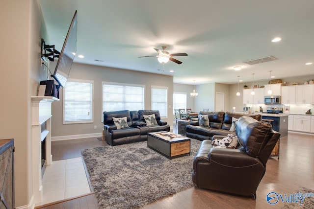 living area featuring recessed lighting, visible vents, a tiled fireplace, wood finished floors, and ceiling fan with notable chandelier