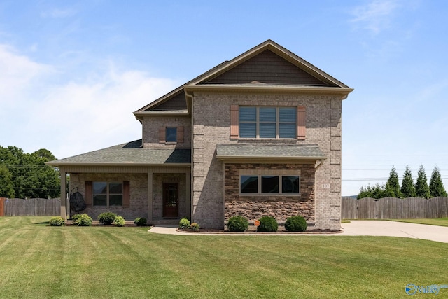 craftsman-style home featuring a front lawn, roof with shingles, fence, and brick siding