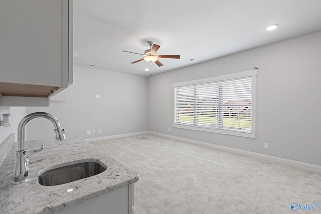 kitchen featuring sink, light carpet, light stone countertops, and ceiling fan