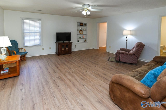 living room featuring built in shelves, light hardwood / wood-style flooring, and ceiling fan
