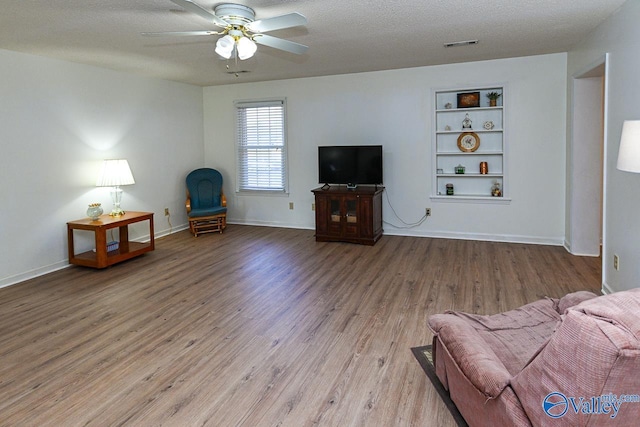 living room featuring ceiling fan, hardwood / wood-style floors, a textured ceiling, and built in shelves