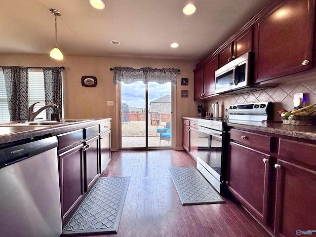 kitchen featuring sink, appliances with stainless steel finishes, hanging light fixtures, backsplash, and dark hardwood / wood-style flooring