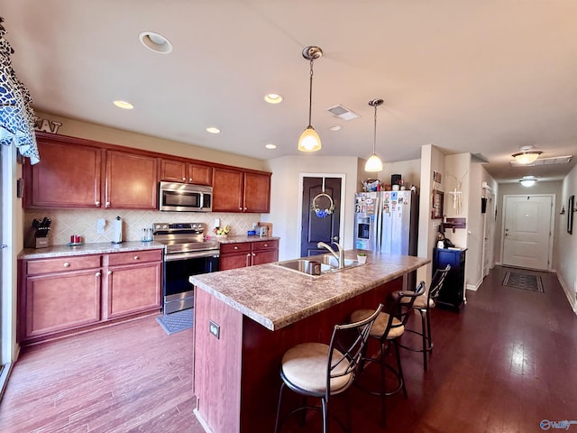 kitchen featuring sink, tasteful backsplash, decorative light fixtures, appliances with stainless steel finishes, and a kitchen island with sink