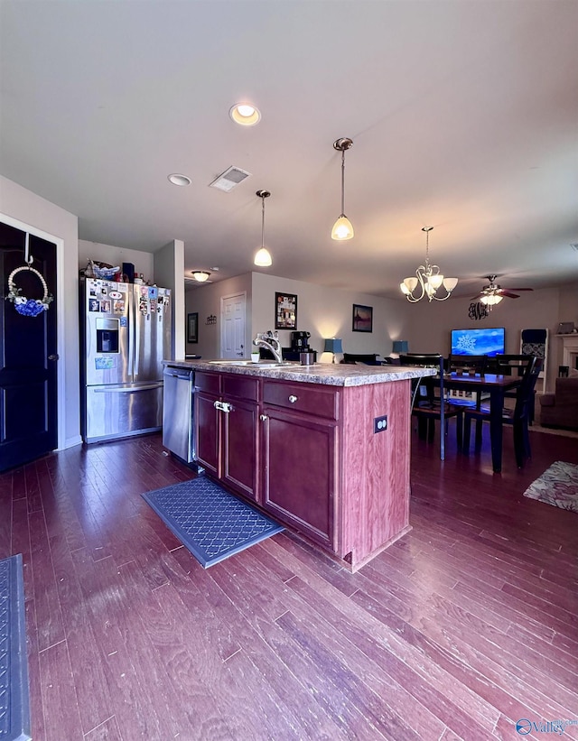 kitchen with appliances with stainless steel finishes, dark hardwood / wood-style flooring, an island with sink, pendant lighting, and ceiling fan