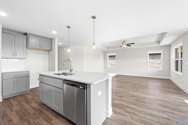 kitchen with sink, gray cabinetry, a center island with sink, stainless steel dishwasher, and a raised ceiling