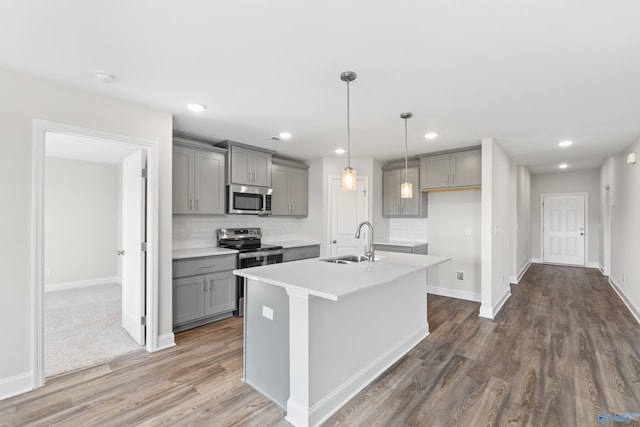 kitchen with sink, appliances with stainless steel finishes, a kitchen island with sink, gray cabinetry, and decorative light fixtures