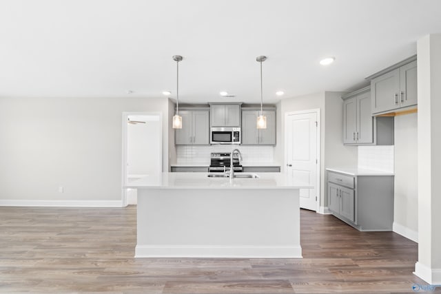 kitchen with appliances with stainless steel finishes, a kitchen island with sink, hanging light fixtures, and gray cabinetry