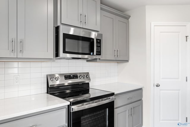 kitchen with stainless steel appliances, gray cabinets, backsplash, and light stone counters