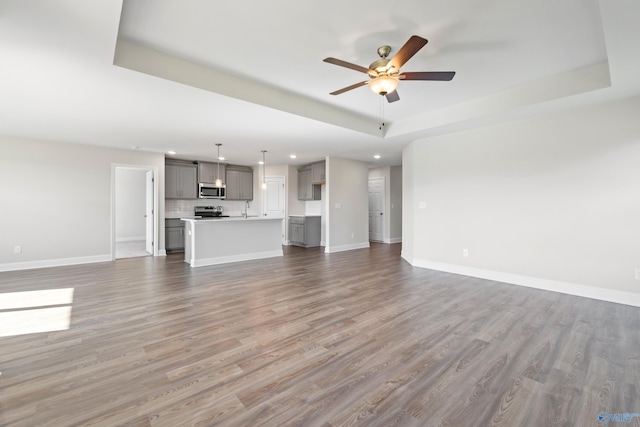 unfurnished living room with a raised ceiling, hardwood / wood-style flooring, sink, and ceiling fan