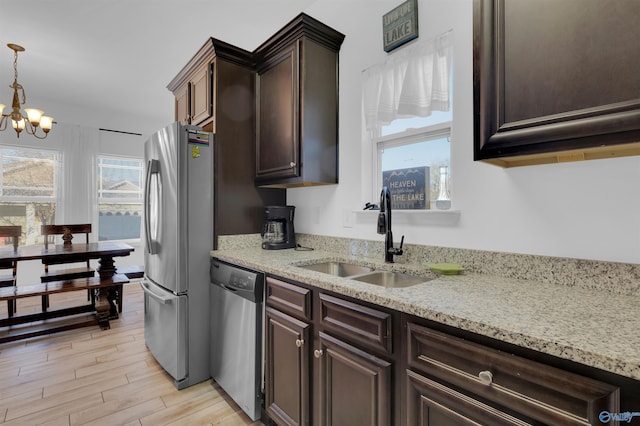 kitchen featuring light stone countertops, dark brown cabinetry, appliances with stainless steel finishes, a notable chandelier, and a sink