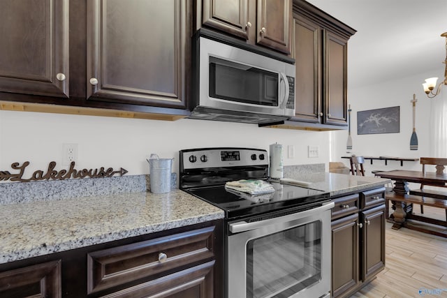 kitchen featuring light stone countertops, dark brown cabinetry, light wood-type flooring, appliances with stainless steel finishes, and an inviting chandelier