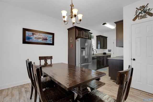 dining space with light wood-style flooring, a notable chandelier, and baseboards