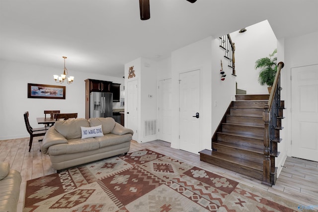 living room featuring stairway, visible vents, light wood-style flooring, and ceiling fan with notable chandelier