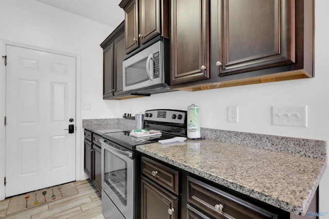 kitchen with dark brown cabinets, light stone countertops, appliances with stainless steel finishes, and wood tiled floor