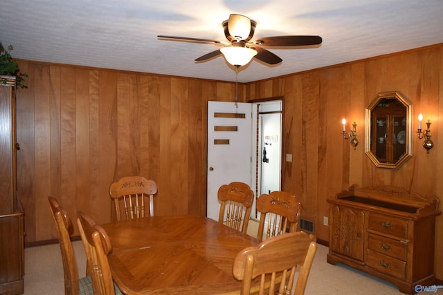 dining room featuring visible vents, light carpet, a ceiling fan, and wood walls