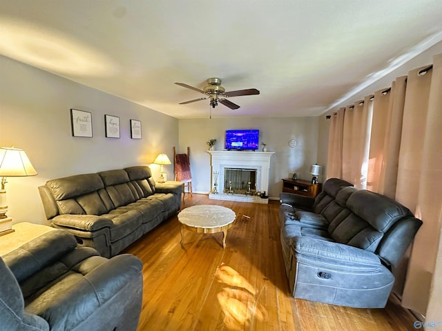living area featuring ceiling fan, wood-type flooring, and a fireplace with raised hearth
