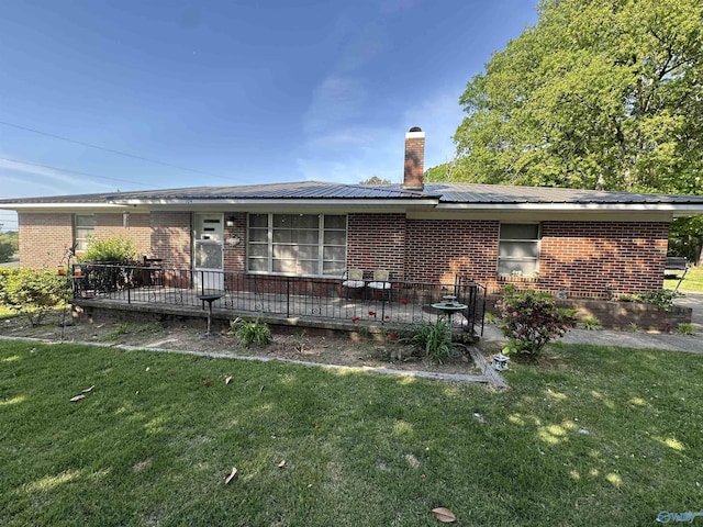 back of property featuring roof mounted solar panels, a chimney, brick siding, and a yard