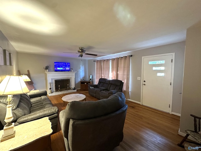 living room featuring baseboards, wood finished floors, a fireplace with raised hearth, and ceiling fan