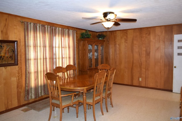 dining area with a ceiling fan, baseboards, wood walls, and light floors