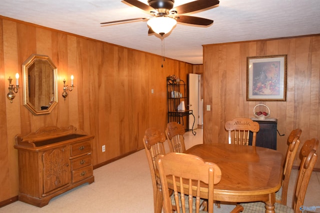 dining area featuring a ceiling fan, wood walls, and light colored carpet