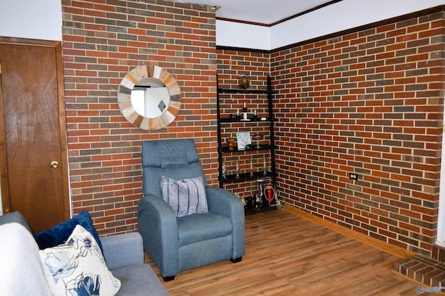 living area featuring brick wall, wood finished floors, and crown molding
