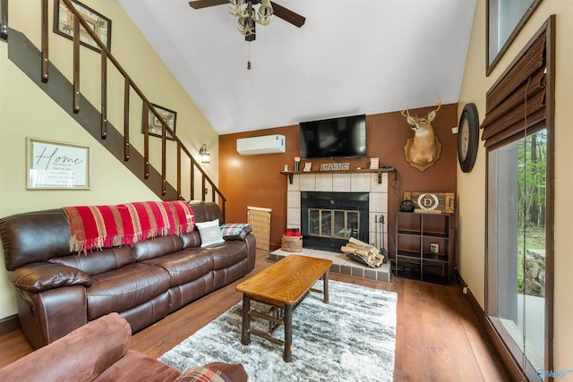 living area with a tile fireplace, ceiling fan, wood finished floors, stairs, and a wall mounted AC