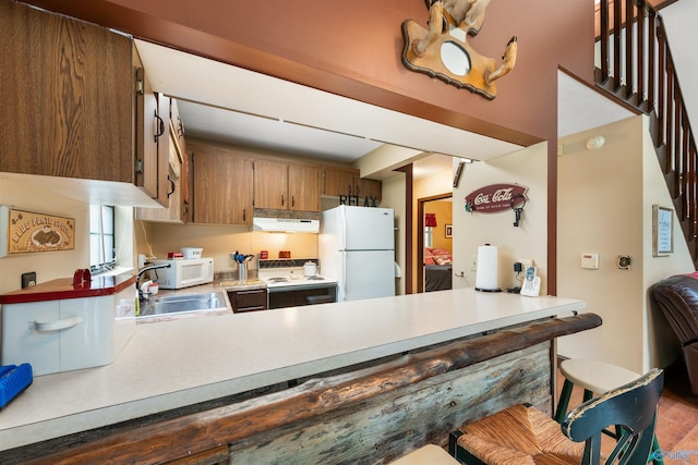 kitchen featuring light countertops, a sink, a peninsula, white appliances, and under cabinet range hood