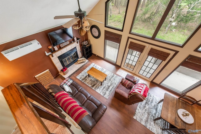 living area with a tiled fireplace, ceiling fan, wood finished floors, french doors, and high vaulted ceiling