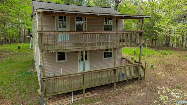 rear view of property featuring a deck, a lawn, and roof with shingles