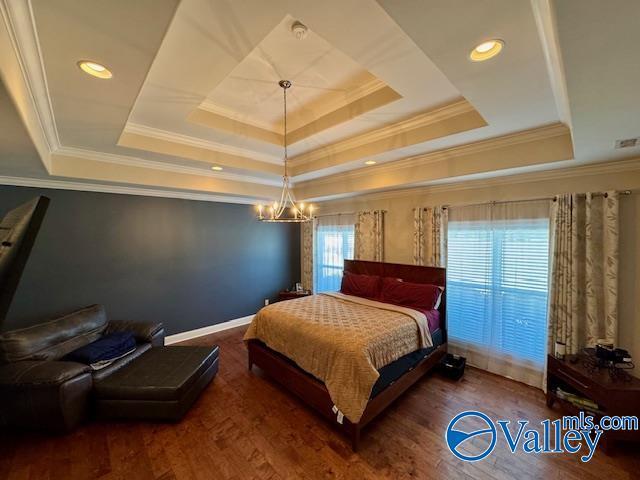 bedroom with ornamental molding, dark hardwood / wood-style floors, a chandelier, and a tray ceiling