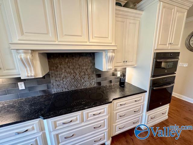 kitchen featuring dark hardwood / wood-style floors, dark stone countertops, white cabinets, backsplash, and black appliances