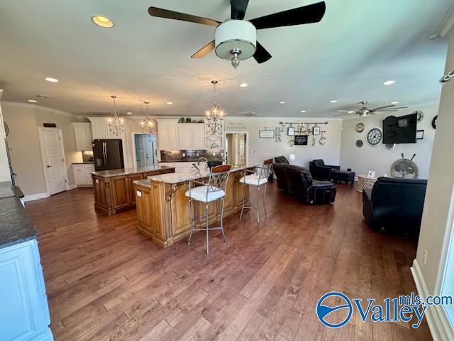 kitchen with decorative light fixtures, a large island with sink, black refrigerator, a kitchen breakfast bar, and white cabinets