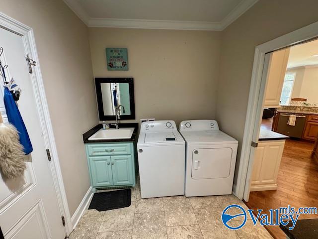 clothes washing area with crown molding, cabinets, separate washer and dryer, and sink