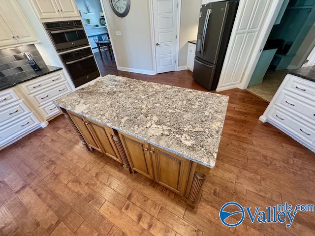 kitchen featuring stainless steel refrigerator with ice dispenser, light stone counters, a center island, dark hardwood / wood-style floors, and white cabinets