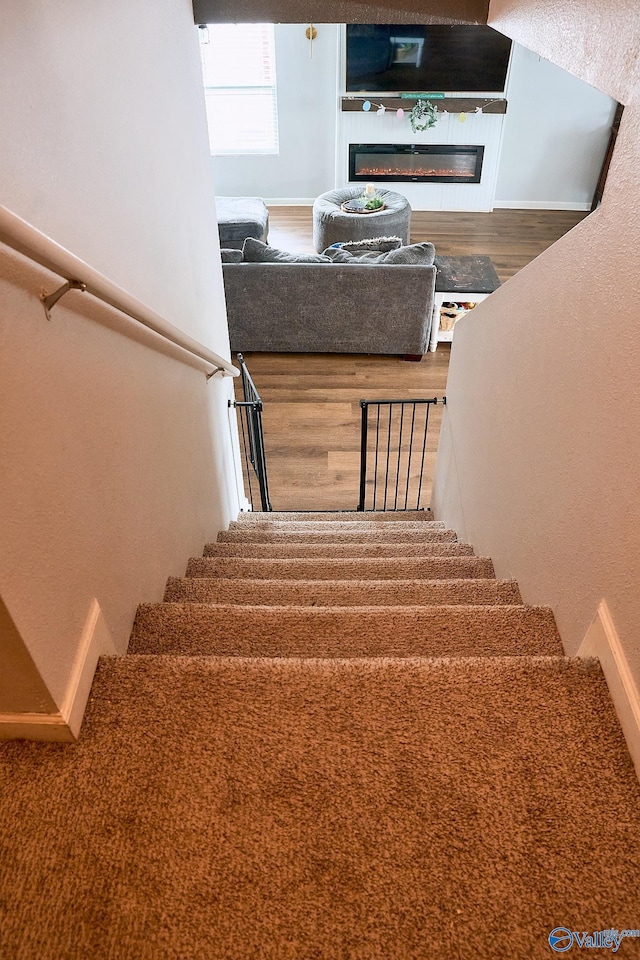 staircase featuring a glass covered fireplace and wood finished floors