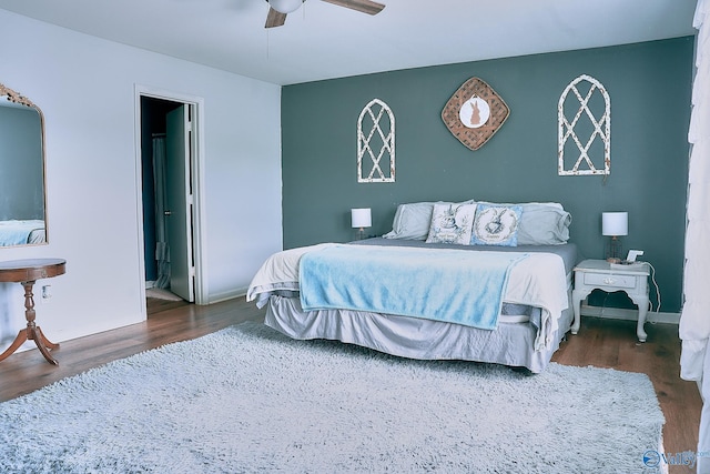 bedroom with baseboards, ceiling fan, ensuite bath, and wood finished floors