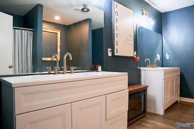 bathroom with baseboards, a sink, two vanities, and wood finished floors