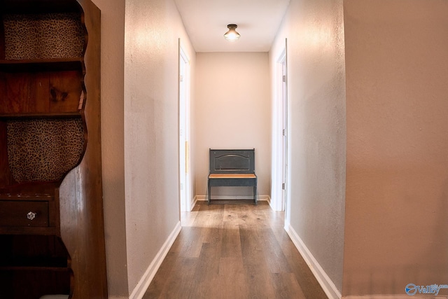 hall with baseboards, a textured wall, and wood finished floors