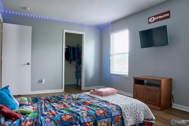 bedroom featuring baseboards, a walk in closet, wood finished floors, and a closet