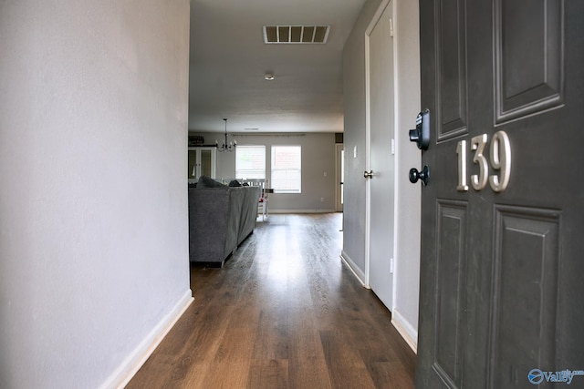 corridor featuring a notable chandelier, baseboards, visible vents, and dark wood finished floors