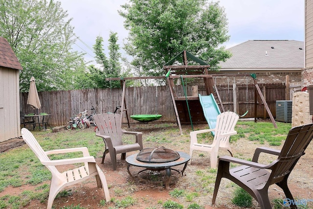view of yard with central AC unit, a fire pit, a fenced backyard, and a playground